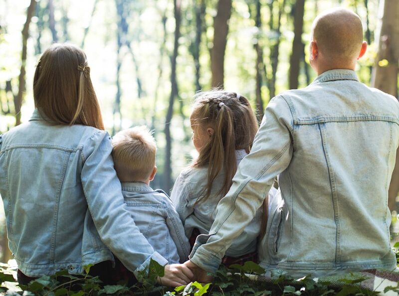 man and woman holding hands together with boy and girl looking at green trees during day